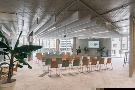 Eventraum mit zwei Bildschirmen, Bühnenaufbau und Sesselreihen vor Fensterfront. Eventraum mit zwei Bildschirmen, Bühnenaufbau und Sesselreihen vor Fensterfront.