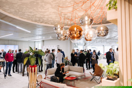 Networking-Event in einem Open Space mit Sitzecke unter modernen Lampen im Vordergrund sowie Kleingruppen in den Eventräumen im Hintergrund. Networking-Event in einem Open Space mit Sitzecke unter modernen Lampen im Vordergrund sowie Kleingruppen in den Eventräumen im Hintergrund.