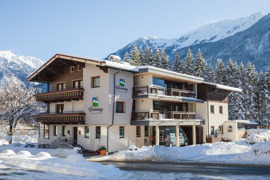 Haus Dschulnigg im Sonnenschein mit schneebedeckten Bergen und Natur im Hintergrund