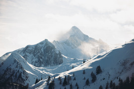 Morgenstimmung auf den verschneiten Bergen rund um das Kitzsteinhorn, mit prominenter Gipfelform im Hintergrund, bew&ouml;lktem Himmel und schneebedeckten H&auml;ngen.