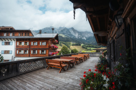 Hotel Puradies, ehemaliges Bauernhaus, liebevoll hergerichtet, mit Blumen am Balkon, im Sommer umgeben von gr&uuml;nen Wiesen und mit Bergen im Hintergrund.
