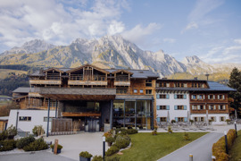 Haupteingang des Hotel Puradies im Sommer, mit gr&uuml;ner Wiese im Vordergrund und Bergkulisse im Hintergrund.