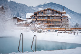 Teil des Hotel Puradies mit sch&ouml;ner Holzfassade im Winter, schneebedeckt, im Vordergrund ein Teil des Au&szlig;en-Infinity-Pools.