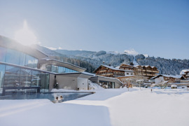 Au&szlig;en-Infinity-Pool im Winter mit zwei Personen darin, im Hintergrund ein Teil des Hotels, umgeben von verschneiter Landschaft.