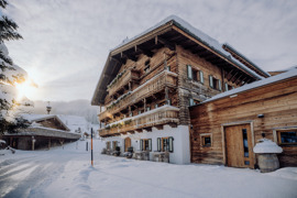 Liebevoll hergerichteter Teil des Hotels, ehemals Bauernhaus, im Winter von Schnee bedeckt, mit dem Eventchalet im Hintergrund.