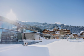 Infinity-Pool im Winter mit zwei Personen, umgeben von Schnee, im Hintergrund das Hotel vor einer verschneiten Winterlandschaft.