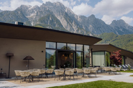 Terrasse des Gourmetrestaurants Essenz im Sommer, im Vordergrund gr&uuml;ne Wiese, im Hintergrund beeindruckende Bergkulisse.