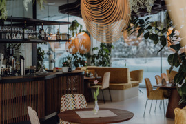 Gourmetrestaurant Essenz mit sch&ouml;n gedeckten Tischen und Glasfront mit Blick auf die Winterlandschaft.