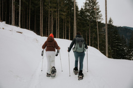 Zwei Schneeschuhwanderer im Winter, von hinten, umgeben von verschneiter Winterlandschaft.