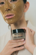 Frau mit nat&uuml;rlicher Gesichtsmaske h&auml;lt einen Tiegel der Mariko Cosmetics Clay Mask in den H&auml;nden &ndash; luxuri&ouml;se Hautpflege inspiriert von asiatischen Beauty-Ritualen.