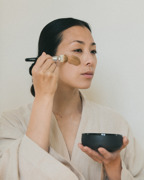 Frau mit nat&uuml;rlicher Gesichtsmaske h&auml;lt einen Tiegel der Mariko Cosmetics Clay Mask in den H&auml;nden &ndash; luxuri&ouml;se Hautpflege inspiriert von asiatischen Beauty-Ritualen.