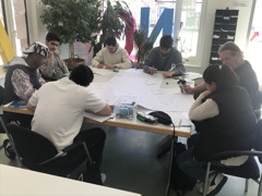 Gruppe von Lernenden sitzt mit Lehrer rund um großen Papierbogen Gruppe von Lernenden sitzt mit Lehrer rund um großen Papierbogen