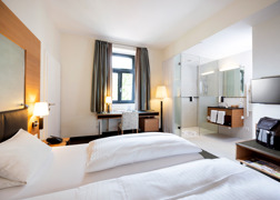 Helles Hotelzimmer im Hotel Sailer mit Doppelbett, Schreibtisch und offenem Badezimmer mit Dusche. Helles Hotelzimmer im Hotel Sailer mit Doppelbett, Schreibtisch und offenem Badezimmer mit Dusche.