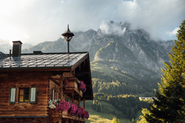 Historisches Bauernhaus als Teil vom Naturresort Puradies mit Blumenbalkon und Bergen im Hintergrund.