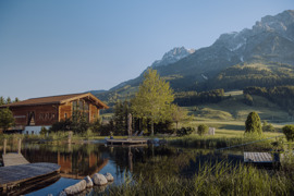 Naturbadeteich im Naturresort Puradies mit Saunahaus und Bergen im Hintergrund.
