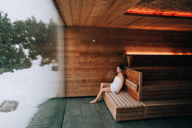 Person in der Sauna im Saunahaus vom Naturresort Puradies mit Blick in die Winterlandschaft.
