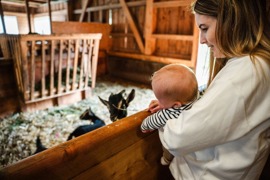 Person mit Baby bei den Ziegen im Stall vom hoteleigenen Bauernhof im Naturresort Puradies.