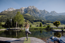 Person beim Yoga am Naturbadeteich vom Naturresort Puradies mit Bergen im Hintergrund.