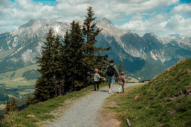 Person mit zwei Kindern beim Wandern in Leogang mit den Leoganger Steinbergen im Hintergrund.