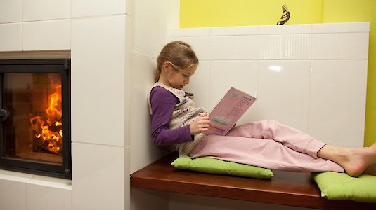 Mädchen liest neben Kachelofen
